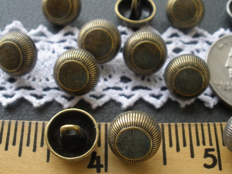 May include: A collection of 10 antique gold-toned metal buttons with a raised, circular design. The buttons have a smooth, slightly textured surface and a shiny finish.
