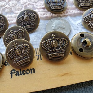 May include: A collection of 10 antique gold-toned metal buttons with a raised crown design. The buttons are approximately 1 inch in diameter.