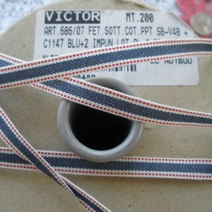 May include: A spool of navy blue and white ribbon with red dotted accents. The ribbon is wrapped around a cardboard spool. The text "VICTOR" and other details are visible on the label.