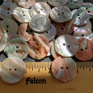 May include: A collection of iridescent mother of pearl buttons with brown and green patterns. The buttons are arranged in a pile and a US quarter is included for scale.