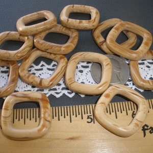 May include: Ten square-shaped, brown and white marbled plastic or wood beads with a hole in the center. The beads are approximately 1 inch in diameter.