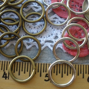 May include: A close-up of two piles of metal rings. One pile is silver and the other is gold. The rings are all about 1 inch in diameter. A ruler is in the background.