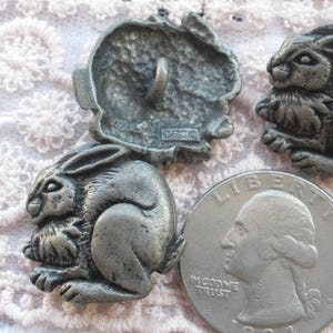 May include: Three pewter buttons featuring a rabbit design. The buttons are detailed and have a textured finish. One button has a smooth back with the word "ORCO" printed on it.