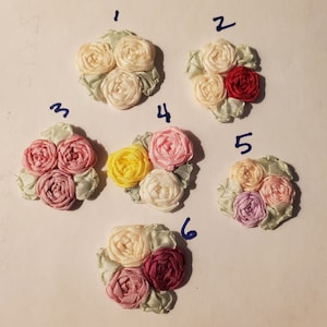 May include: Six different fabric flower embellishments, each with three flowers in a cluster. The flowers are in various colors, including pink, red, yellow, white, and purple.