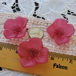 May include: Four pink flower-shaped objects with a quarter coin and a wooden ruler. The flowers have a textured surface and a darker center. The ruler is marked with inches and the word "falcon".