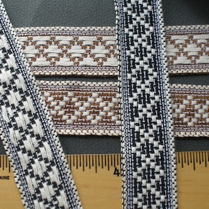 May include: Close-up of woven ribbons in various patterns. One ribbon features a black and white checkered design, while others display a brown and cream geometric pattern. The ribbons are placed next to a ruler.