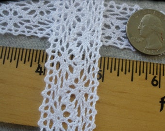 May include: Close-up of white lace trim with an openwork design. A wooden ruler with inch markings and a US quarter coin are next to the lace. The lace is approximately 1 inch wide.