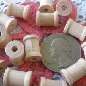 May include: A collection of wooden spools in various sizes, scattered on a white lace doily with a pink floral design. A US quarter is included for scale.