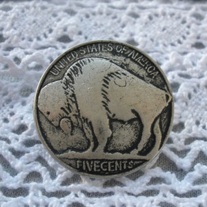 May include: A silver-colored nickel coin with the image of a buffalo and the text "United States of America" and "Five Cents".