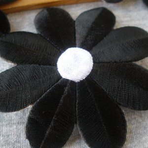 May include: Black velvet flower applique with a white center. The flower has seven petals and is about 3 inches in diameter.