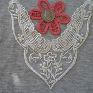 May include: White lace trim with a delicate floral design and a pink flower in the center.