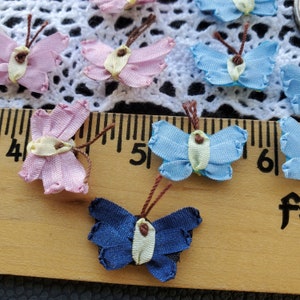 May include: Assortment of small fabric butterflies in pink, blue, and navy blue colors. The butterflies are arranged on a wooden ruler with inch markings.