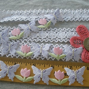 May include: A collection of lavender and pink embroidered butterflies and tulips. The butterflies have silver glitter accents. The appliques are arranged on a white lace trim and a wooden ruler.