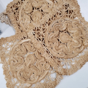 May include: A set of light brown crocheted doilies featuring an intricate, raised, swirling cord-like pattern arranged in circular motifs. The openwork design is created with fine thread, showcasing a textured, interconnected, and lace-like structure.