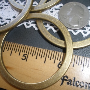 May include: A set of five brass rings, each with a slightly different diameter, are arranged on a wooden ruler with the text "Falcon" printed on it. The rings are all about 2 inches in diameter.