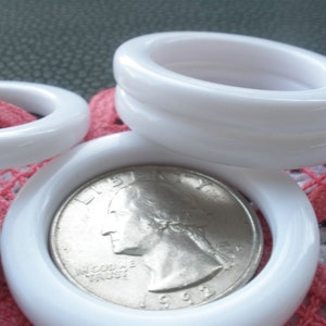 May include: A set of four white plastic rings, stacked on top of each other. The rings are smooth and glossy. A silver US quarter is resting inside one of the rings.