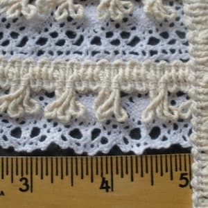 May include: White crochet trim with a fringe detail, measured with a ruler marked in inches.