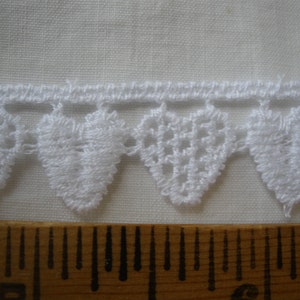 May include: White crocheted lace trim with a scalloped edge and a repeating heart design. The lace is approximately 1 inch wide.
