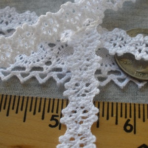 May include: White crochet lace trim with a scalloped edge. The lace is shown next to a ruler, with the trim measuring approximately 5 inches in length.