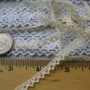 May include: Two pieces of white lace trim with a scalloped edge. The lace is laid out on a wooden ruler with the numbers 2, 3, 4, 5, and 6 visible. A silver US quarter is also visible.