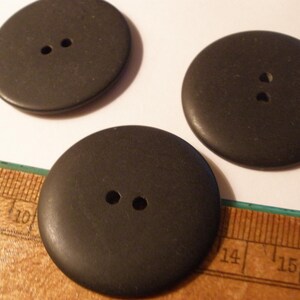 May include: Three large, dark brown buttons with two holes each. The buttons are round and appear to be made of wood or a similar material. A ruler is partially visible in the image, providing scale.