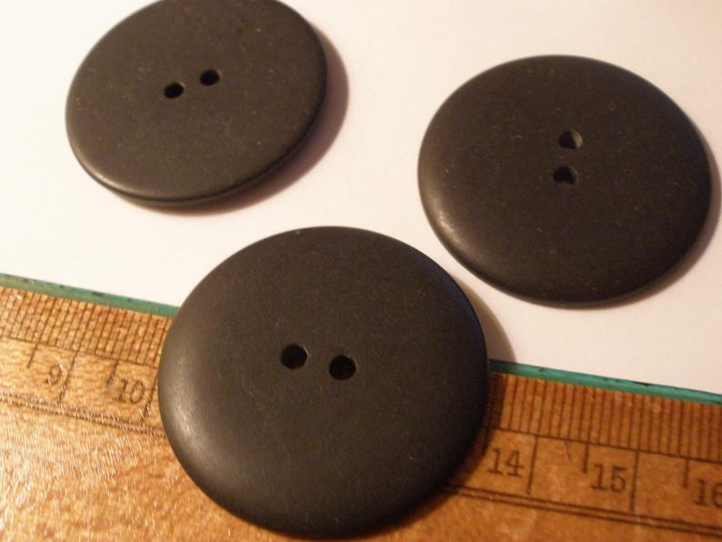 May include: Three large, dark brown buttons with two holes each. The buttons are round and appear to be made of wood or a similar material. A ruler is partially visible in the image, providing scale.