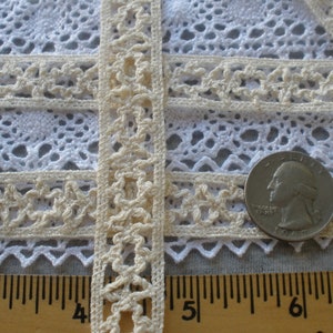 May include: Close-up of ivory crochet lace trim with a scalloped edge. The lace is shown next to a ruler with inches marked. The lace is approximately 1 inch wide.