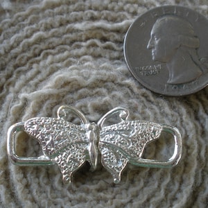 May include: Silver butterfly-shaped toggle clasp with two loops. The clasp is about the size of a US quarter.