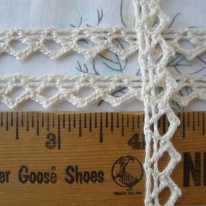 May include: White crochet trim with a delicate diamond pattern. The trim is measured against a wooden ruler with the words "Mother Goose Shoes" printed on it.