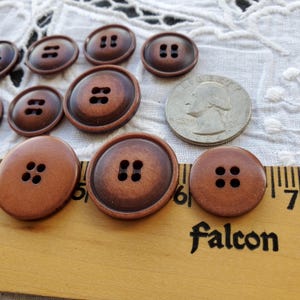 May include: A collection of ten brown plastic buttons with four holes each. The buttons are arranged in a semi-circle on a wooden ruler with the words "Falcon" printed on it. A silver US quarter is also in the image for size comparison.