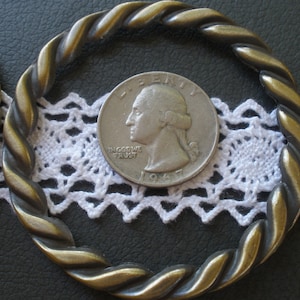 May include: A silver 1967 quarter with the words "Liberty" and "In God We Trust" on it, surrounded by a gold-colored twisted metal ring.