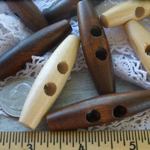 May include: A collection of wooden toggle buttons in brown and natural wood tones. The buttons have two holes and are shaped like a boat.