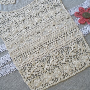 May include: A white crocheted lace trim with a delicate floral pattern. The trim is made of a fine, lightweight material and has a soft, flowing texture.