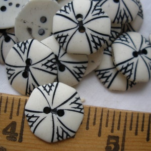 K&ouml;nnte beinhalten: Nahaufnahme eines Stapels wei&szlig;er Kn&ouml;pfe mit schwarzen geometrischen Mustern. Die Kn&ouml;pfe sind in einem zuf&auml;lligen Muster angeordnet und alle gleich gro&szlig;. Ein Holzliniall ist im unteren Teil des Bildes sichtbar.