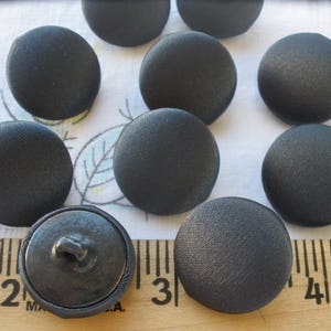 May include: Ten black fabric buttons with a smooth, satin-like finish. The buttons are round and have a diameter of approximately 1 inch.
