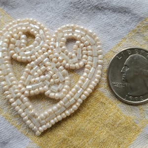 May include: A white beaded heart-shaped embellishment, approximately the size of a quarter.