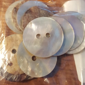 May include: A package of 10 round, white, mother-of-pearl buttons with two holes each. The buttons are in a clear plastic bag with a white backing card.