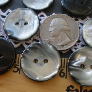 May include: A collection of 10 black and white swirl buttons. The buttons are approximately 1 inch in diameter and have two holes. The buttons are arranged on a white lace doily with a US quarter for scale.
