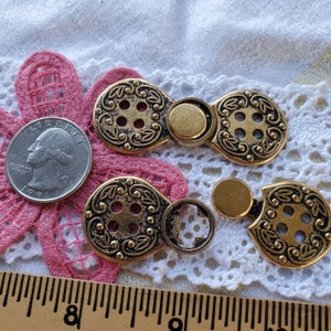 May include: Two gold-toned metal button closures with intricate designs and a decorative button in the center. The closures have a loop on one side and a button on the other.
