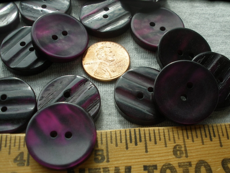 K&ouml;nnte beinhalten: Eine Sammlung von 15 dunkelvioletten Kn&ouml;pfen mit einem gestreiften Muster. Die Kn&ouml;pfe haben zwei L&ouml;cher und sind etwa 2,5 cm im Durchmesser.