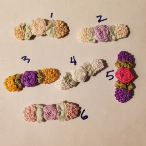 May include: Six different fabric flower embellishments with numbers 1 through 6 written next to them. The flowers are made of satin ribbon and are in various colors, including pink, purple, white, and green.
