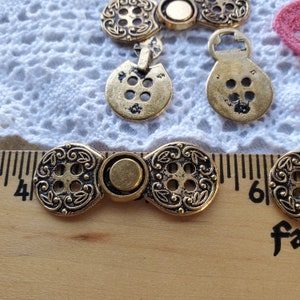 May include: A set of gold-toned metal buttons with intricate floral designs and a button closure. The buttons are arranged on a white lace fabric and a wooden ruler with the numbers 4 and 6 visible.