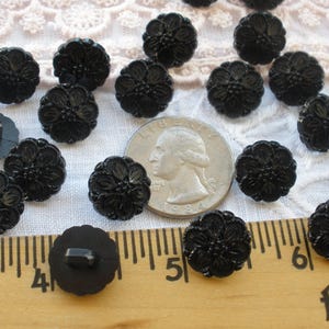 May include: A collection of 18 black plastic buttons with a floral design. The buttons are approximately 1 inch in diameter and have a shank back.