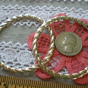 May include: Two silver twisted wire hoops, one slightly larger than the other, on a pink and white floral fabric background. A quarter is included for size reference.