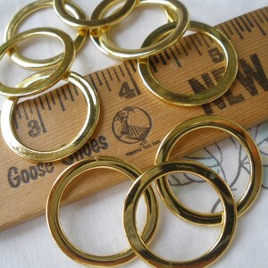 May include: A group of gold-colored metal rings of various sizes. The rings are arranged on a wooden ruler with the words "Mother Goose Shoes" and "New York" printed on it.