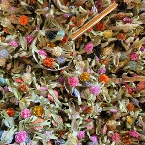 May include: A close-up image of a variety of colorful fabric flowers and ribbons. The flowers are arranged in a random pattern and are surrounded by a silver spoon. The spoon is filled with more flowers and ribbons.