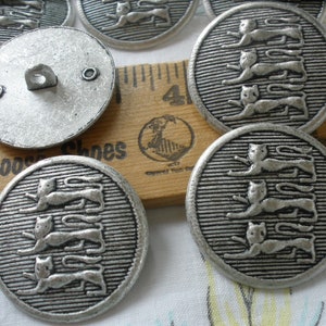 May include: Silver metal buttons with a design of three cats walking in a line. The buttons have a textured surface and a shiny finish.