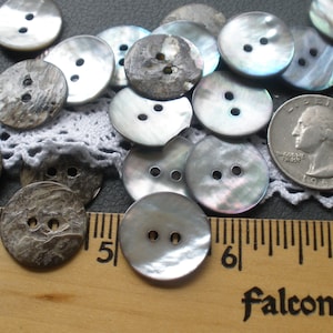 May include: A collection of 20 iridescent mother of pearl buttons with two holes each. The buttons are various shades of gray and blue. A US quarter is included for size reference.