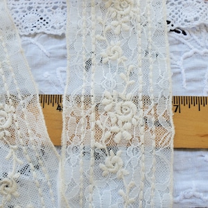 May include: White lace trim with a floral pattern. The lace is delicate and has a soft, vintage feel. It is approximately 1 inch wide.