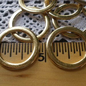 May include: A close-up of a group of gold metal rings, some stacked on top of each other. The rings are lying on a wooden ruler with black markings. The ruler is marked with the numbers 4 and 5.